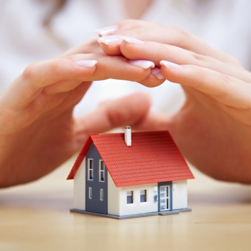 Weibliche Hände schützen ein kleines Einfamilienhaus